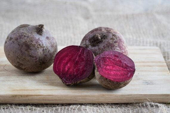 red beets on a cutting board, with one sliced in half to show the bright magenta interior