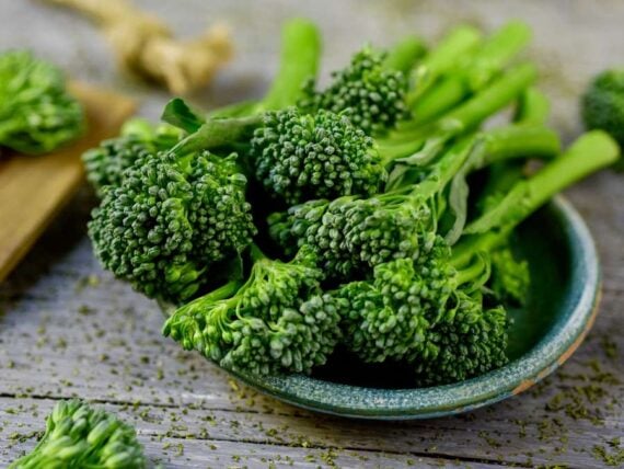 close up of broccolini, or baby broccoli stalks on a small dish on a wooden table